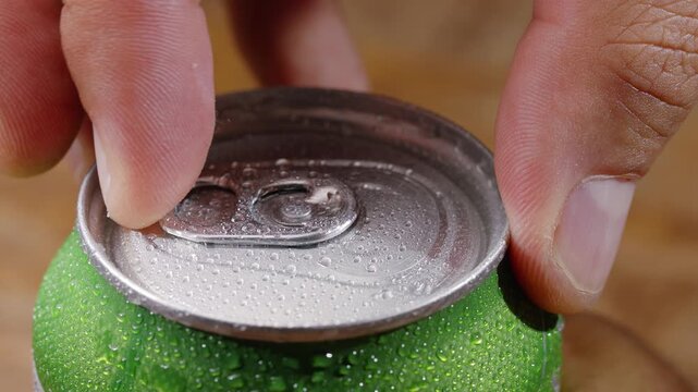 Macro shot of a hand opening a cold aluminum can of carbonated drink covered with water droplets. Perfect for refreshing summer concepts, commercial use, and product promo.