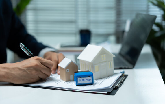 Real estate businessman reviewing approved property documents with house models and laptop, representing mortgage approval, home financing, loan application and property purchase process.