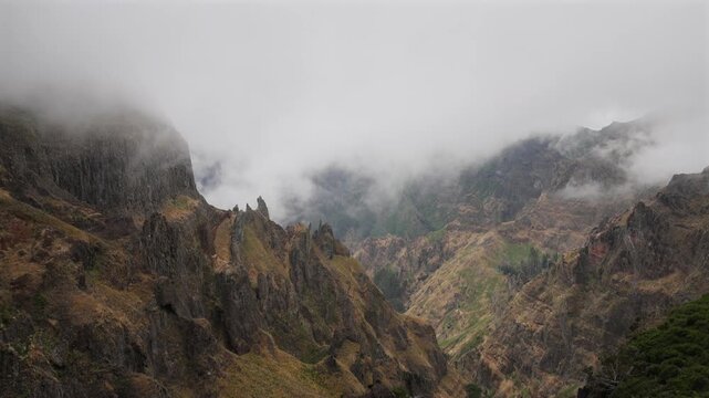 Dramatic foggy mountain peaks and deep volcanic valleys in Madeira under moody overcast sky, showing pristine wilderness, rugged nature and misty atmospheric landscape. 4K video.