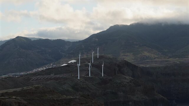 Wind turbines generating clean renewable energy on the dramatic coastal mountain cliffs of Madeira under soft overcast sky light for sustainability concept. 4K video.