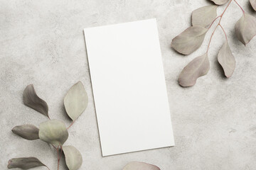 Blank wedding menu card mockup placed on a textured gray surface surrounded by soft green eucalyptus leaves for elegant design presentations © nikavera