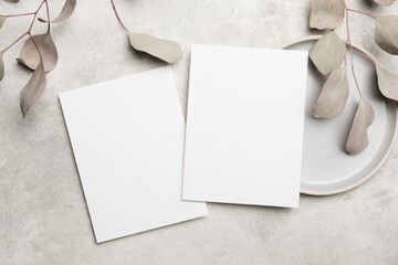 Naklejka premium Blank white stationery sheets placed on a light gray surface with dried eucalyptus leaves and a round ceramic plate in a minimalistic arrangement