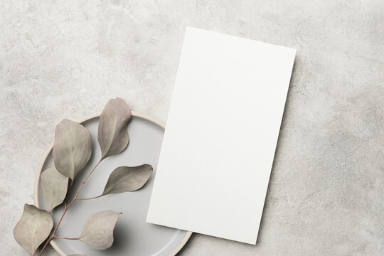 Blank white card mock up on a gray plate with soft green leaves, creating a minimalist and elegant presentation for design purposes and showcasing natural elements