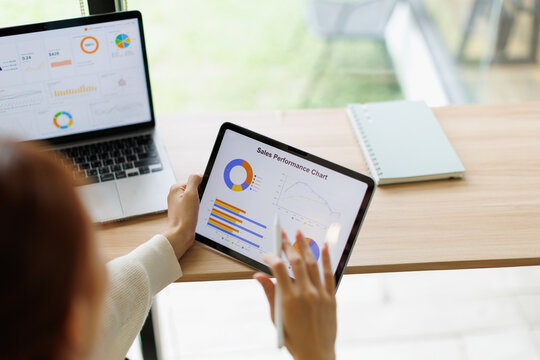 Business professional analyzing sales performance charts and data on a digital tablet and laptop, collaborating on strategy, marketing analytics, and financial reports