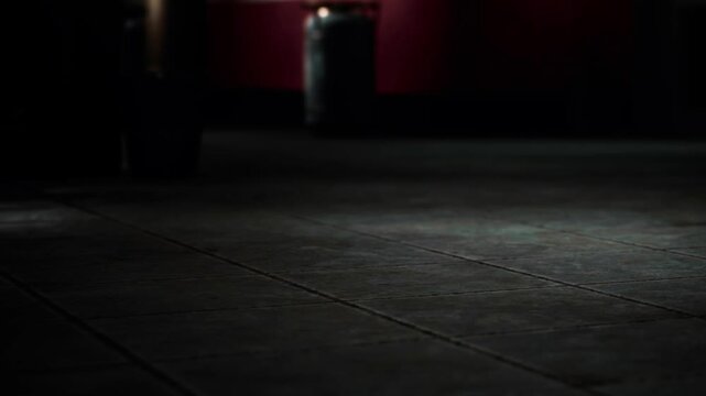 A close up view of a tiled floor in a dimly lit room. Shadows play across the floor tiles, and some light illuminates parts of the surface. The space feels empty and quiet.