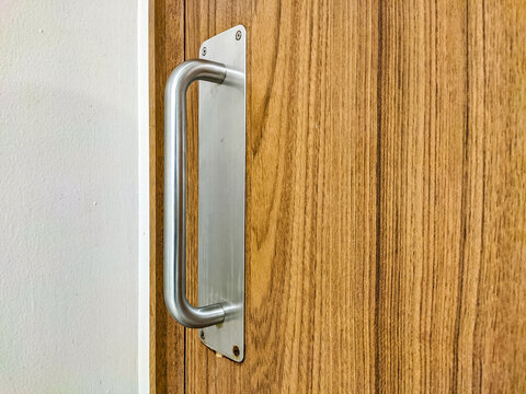 Metal door handle mounted on a wood-pattern HPL door, combining durability and modern design, highlighting clean lines and functional detail in a contemporary interior setting.