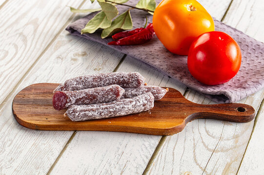 Mini fuet sausages on wooden cutting board with fresh tomatoes and chili peppers
