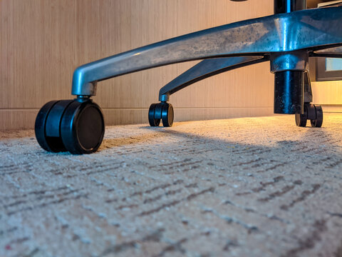 Close-up of metal chair wheels resting on a carpeted indoor floor, highlighting mobility, texture contrast, and practical furniture design in a modern interior setting.