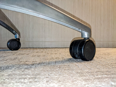 Close-up of metal chair wheels resting on a carpeted indoor floor, highlighting mobility, texture contrast, and practical furniture design in a modern interior setting.