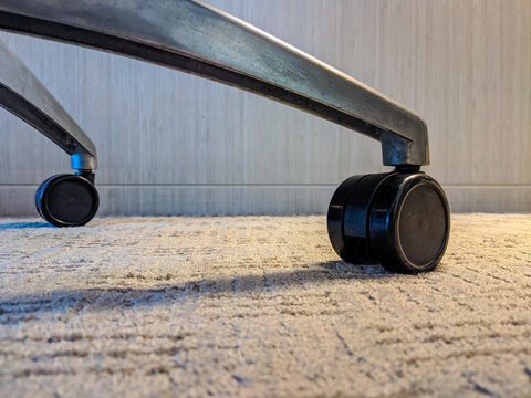 Close-up of metal chair wheels resting on a carpeted indoor floor, highlighting mobility, texture contrast, and practical furniture design in a modern interior setting.