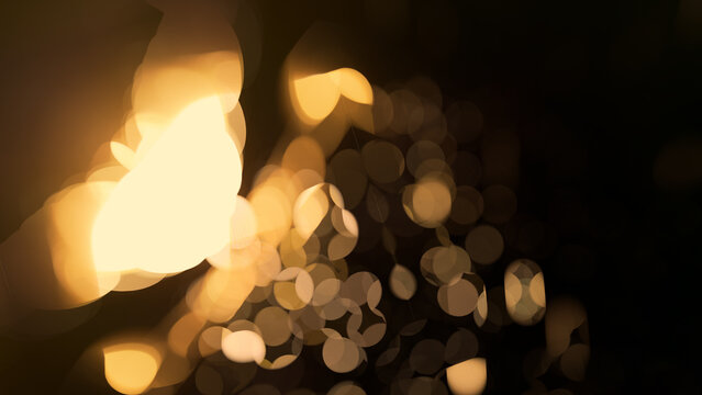 Abstract golden bokeh light dots with warm blurred flare on dark background for luxury holiday banner or festive party decoration