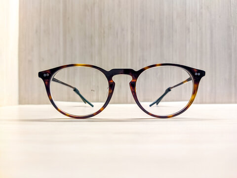 Tortoiseshell eyeglasses resting on a wooden surface, featuring a classic round frame design and subtle reflections, highlighting everyday eyewear with a clean and minimalist composition.