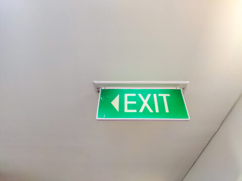 Green illuminated EXIT sign mounted on a corridor ceiling, providing clear emergency wayfinding and directional guidance for people inside a modern building.