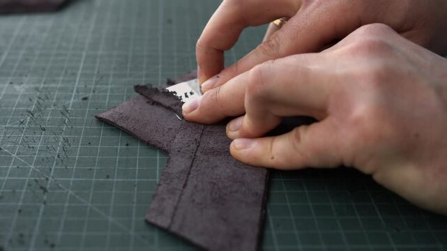 Craftsman skiving leather with a sharp blade in a workshop for handcrafted goods manufacturing