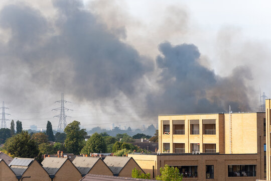 Thick Black Smoke Rising Over Residential Area With Industrial Buildings and Trees