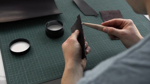 Leather craftsman applying burnishing gum to the edge of a leather piece with a wooden slicker in his workshop