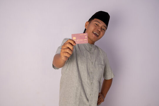 Cheerful Young Man Displaying a Credit Card in a Stylish Attire Against a Light Background