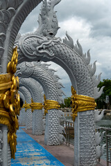 Fototapeta premium Row of Naga serpent statues with golden accents on a cloudy day