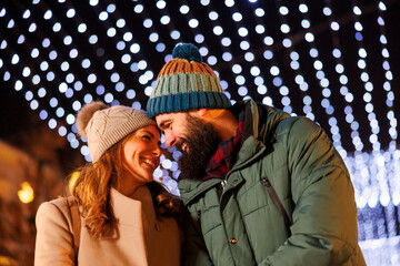 Obraz premium Couple hugging and walking down decorated city streets at Christmas