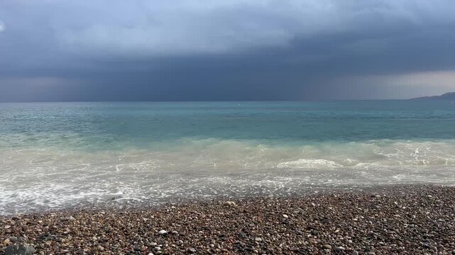 Sea waves crashing on pebble beach under dark stormy sky horizontal video frame