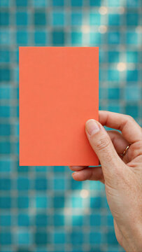 Hand holding blank coral card against checkered background