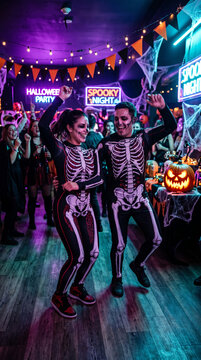 People in skeleton costumes dancing at a Halloween party with pumpkins and cobwebs, symbolizing a festive and spooky celebration.