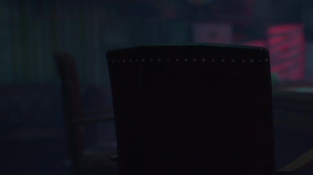 A chair is placed in a dim room. Colorful lights glow in the background. Various objects can be seen, giving a sense of a casual space.