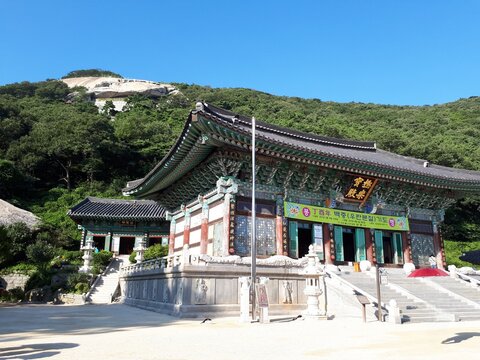 A comprehensive temple view of Bomunsa on Nakgasan Mountain, featuring ornate main halls with intricate dancheong and a majestic granite cliff face in the background. Traditional tiled roofs and woode