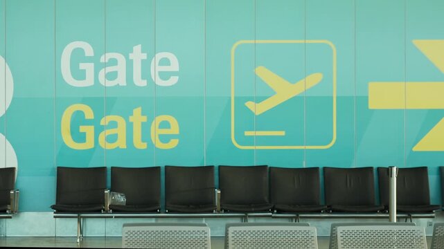 Empty airport terminal gate lounge features rows of seats along modern wall. Clean departure waiting hall offers comfortable transit area for travelers. Modern public aviation hub interior.