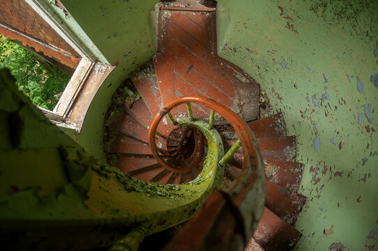 Abandoned overgrown mansion with spiral staircase, old car and ruined interior