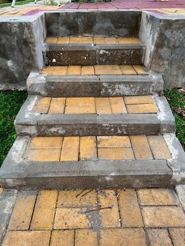 Close-up view of weathered outdoor concrete steps paved with yellowish brick tiles.
