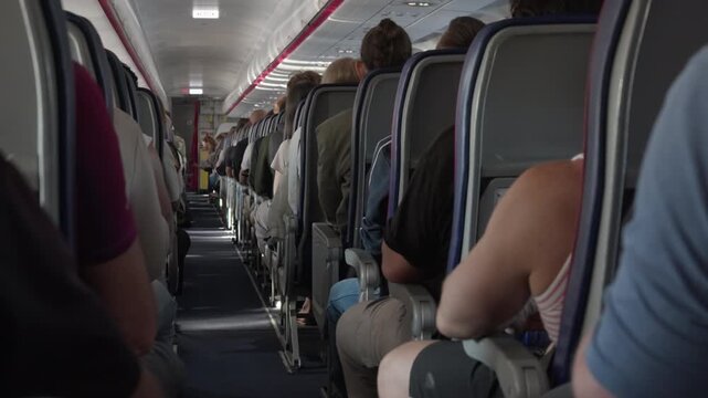 Passengers sit in crowded economy class seats inside an airplane cabin during a budget flight. Many tourists travel on an airliner. Low cost commercial aviation passenger transportation.