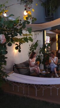 Two female friends drinking juice in a relaxed backyard patio