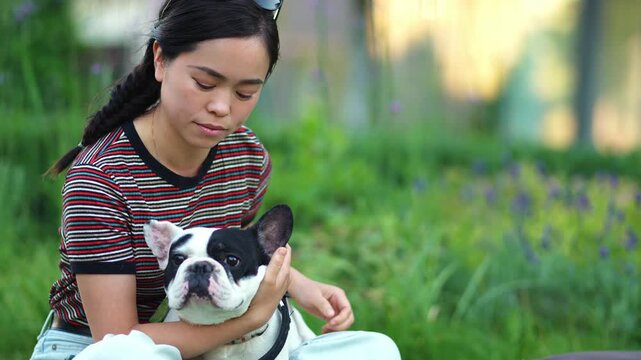 Affectionate japanese woman kissing her french bulldog in the park