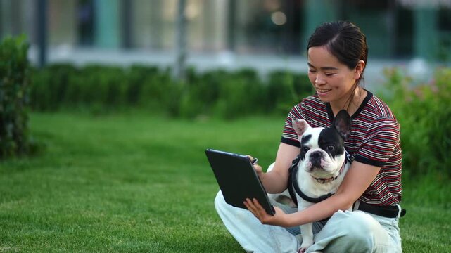 Japanese woman using a tablet with her dog in the park