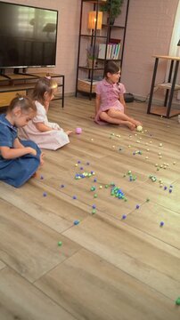 Three little girls playing with marbles on the living room floor