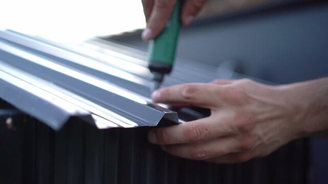 Construction worker fastening corrugated metal roof sheeting with electric screwdriver