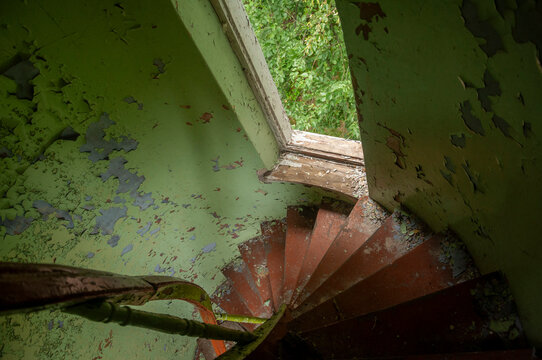 Abandoned overgrown mansion with spiral staircase, old car and ruined interior