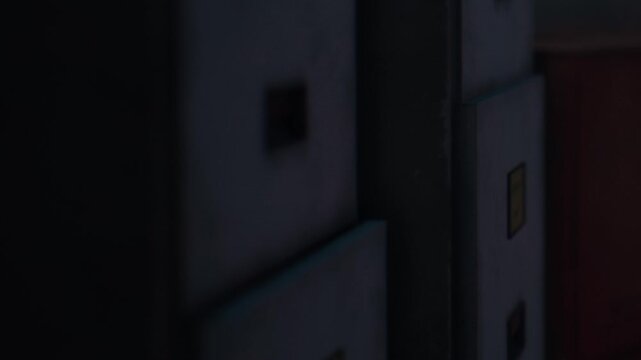 In a dark space, several boxes and containers are arranged close together. Shadows are visible, creating a low light atmosphere that obscures details.