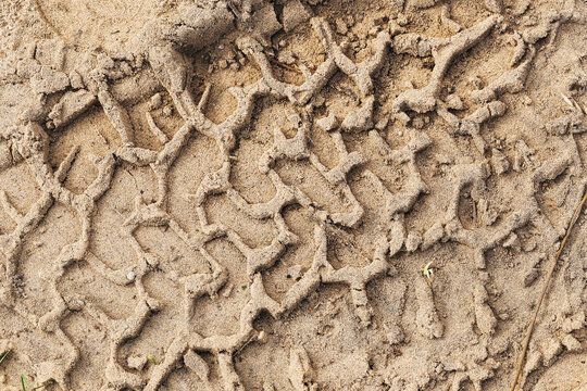 Deep tire tread imprints in dry sandy soil forming repeating rugged pattern. Off road vehicle track texture compacted earth wheel marks terrain detail and natural ground background.