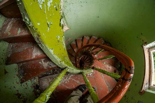 Abandoned overgrown mansion with spiral staircase, old car and ruined interior