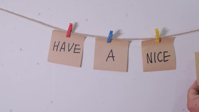 Hand hanging HAVE A NICE DAY message written on craft paper notes with colorful wooden pegs