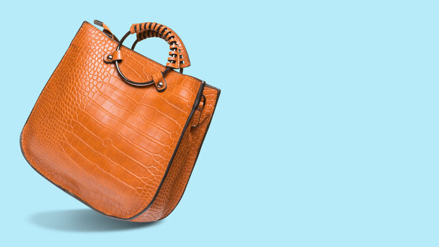 Classic tan brown crocodile pattern leather handbag on light blue background with copy space. Modern womens tote bag side view