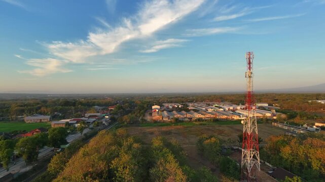 Drone flying forward revealing cell phone antenna and factory complex during golden hour