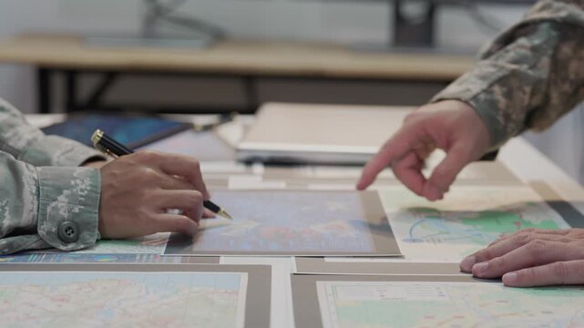 Military officers analyzing tactical map documents and digital tablet in command war room