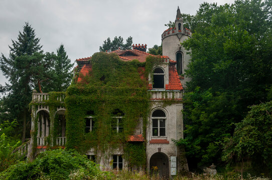 Abandoned overgrown mansion with spiral staircase, old car and ruined interior