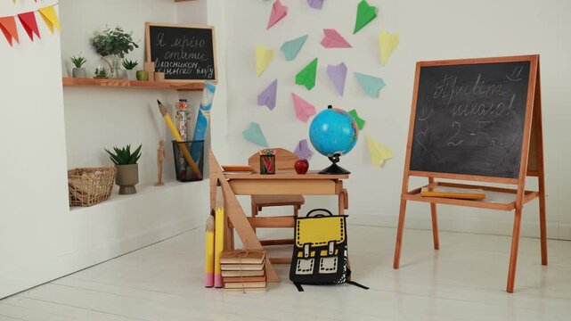 Empty primary interior school classroom setup with wooden desk, globe, apple, chalk board easel. Back to school concept, colorful paper airplanes wall decor, study background, and school supplies.
