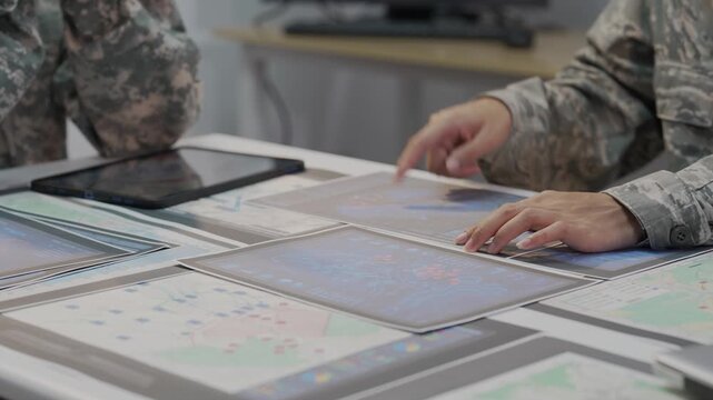 Military officers analyzing tactical map documents and digital tablet in command war room