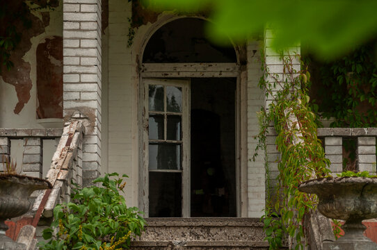 Abandoned overgrown mansion with spiral staircase, old car and ruined interior