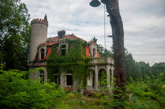 Abandoned overgrown mansion with spiral staircase, old car and ruined interior